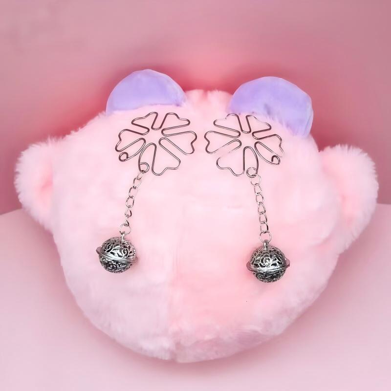 Silver bell nipple jewelry displayed on a pink plush surface for lifestyle aesthetic presentation.