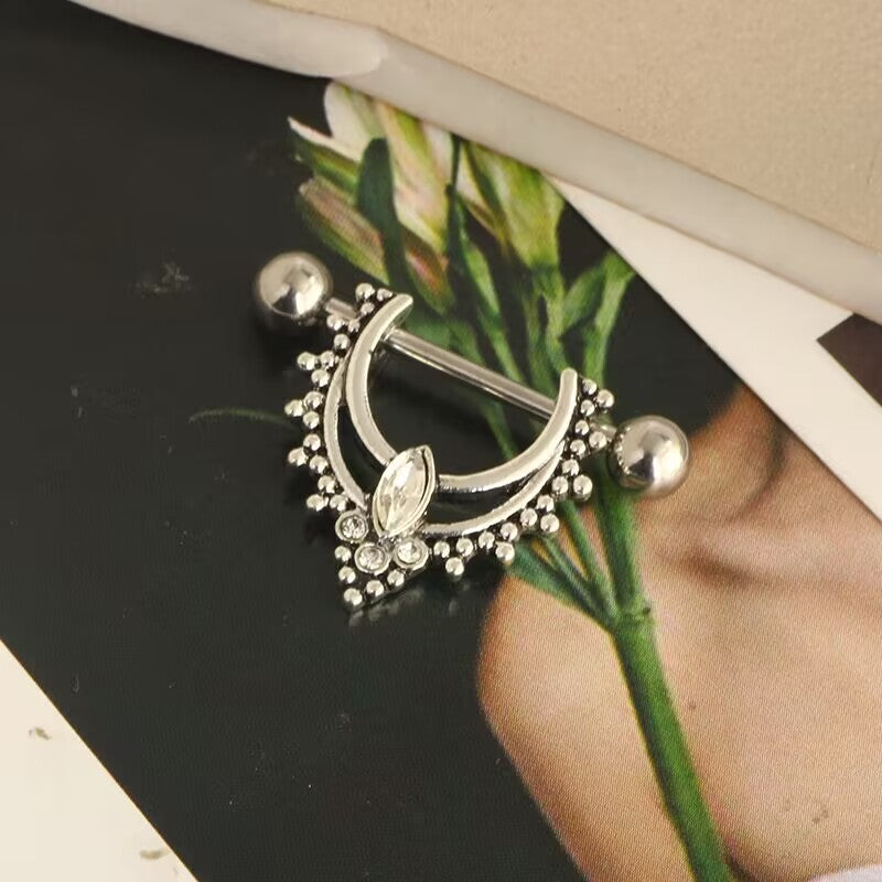 Close-up shot of a single marquise gemstone nipple piercing shield placed near a floral decorative element.