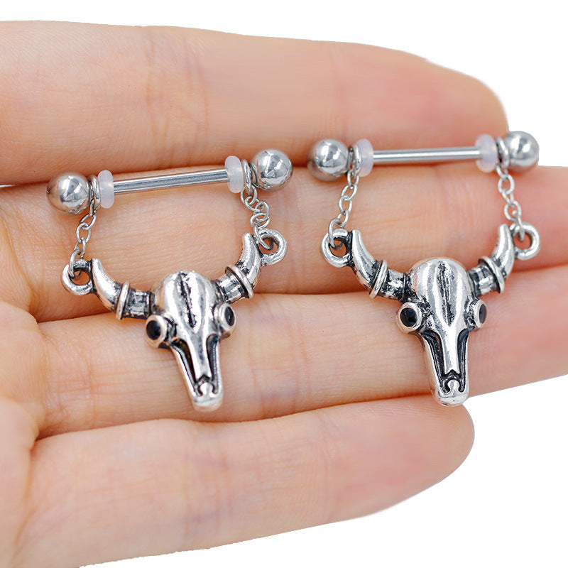 Close-up of a person holding a pair of antique silver bull skull nipple barbells to show scale and detail.
