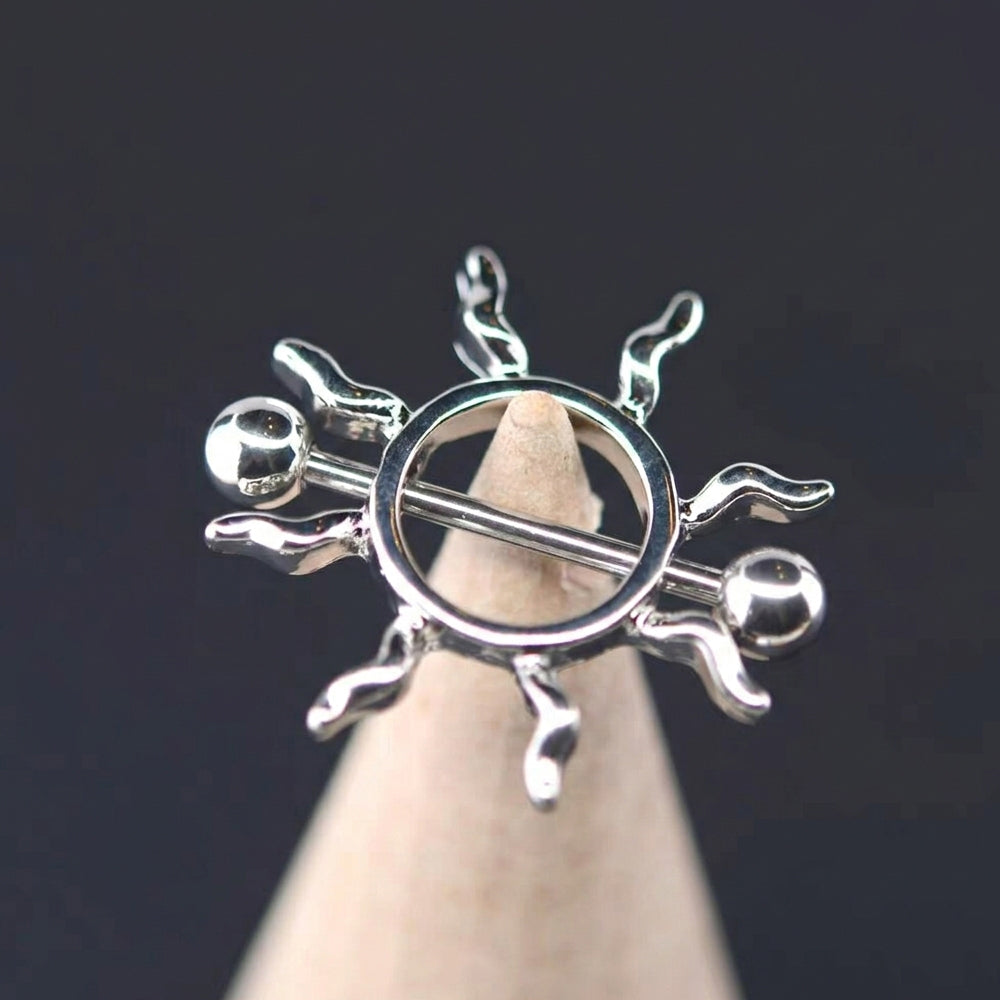 A detailed close-up of a high-polish, sun-shaped nipple shield ring with wave-like rays and smooth end balls, resting on a beige cone shape against a dark background.