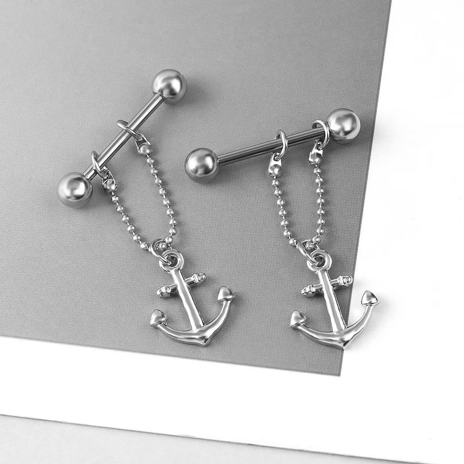 Two anchor dangle nipple barbells displayed on a stylish grey and white background