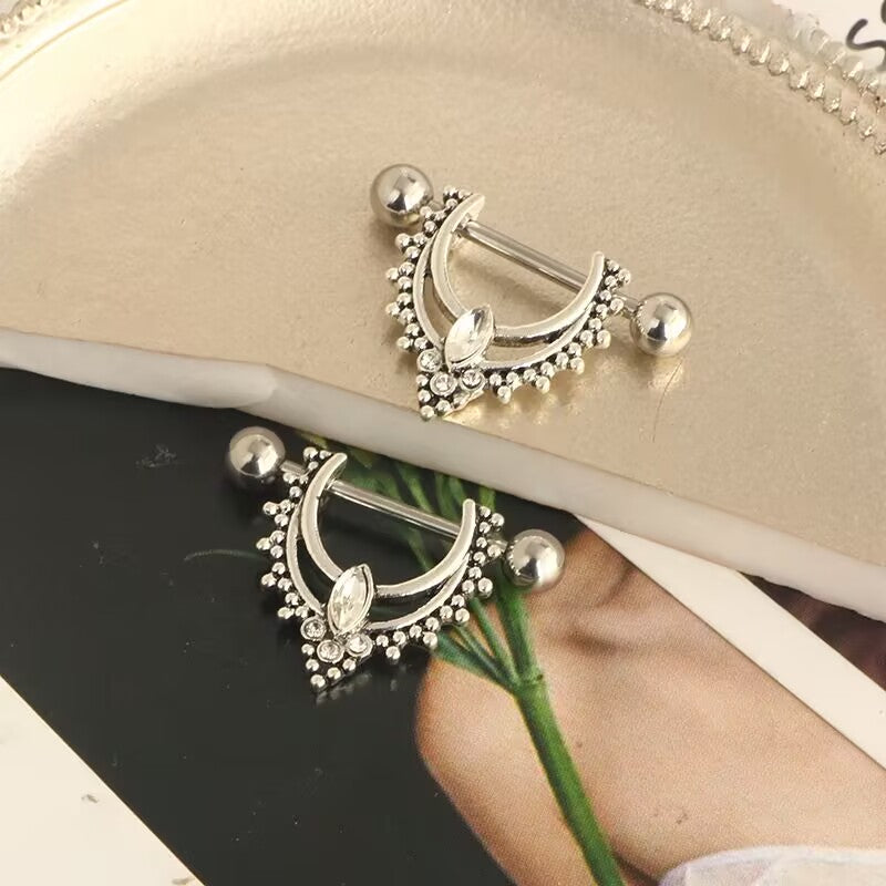 Two gothic nipple shields displayed on an aesthetic surface, showing the detailed craftsmanship and shine.