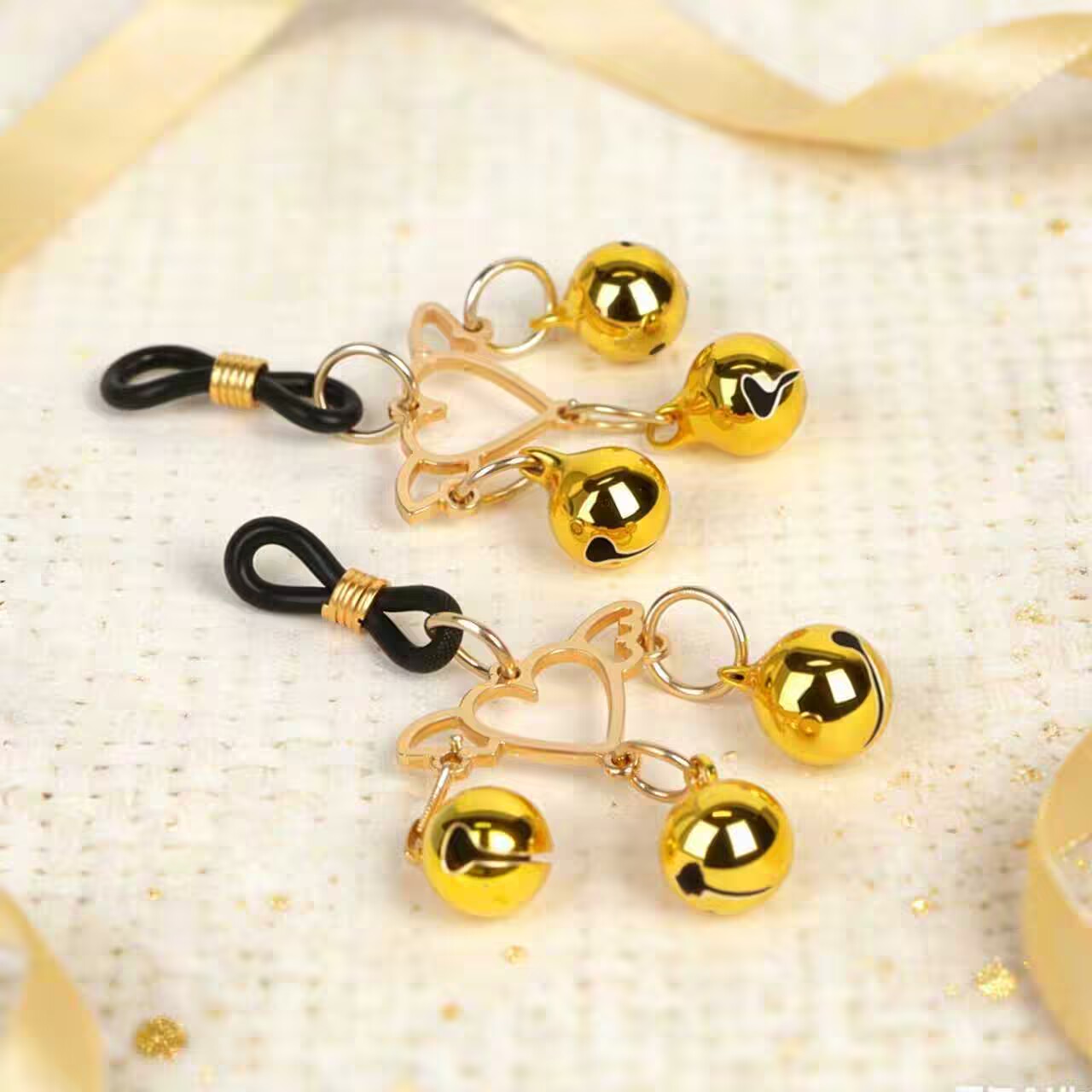 Decorative winged heart nipple clamps placed on a textured surface with golden ribbons.