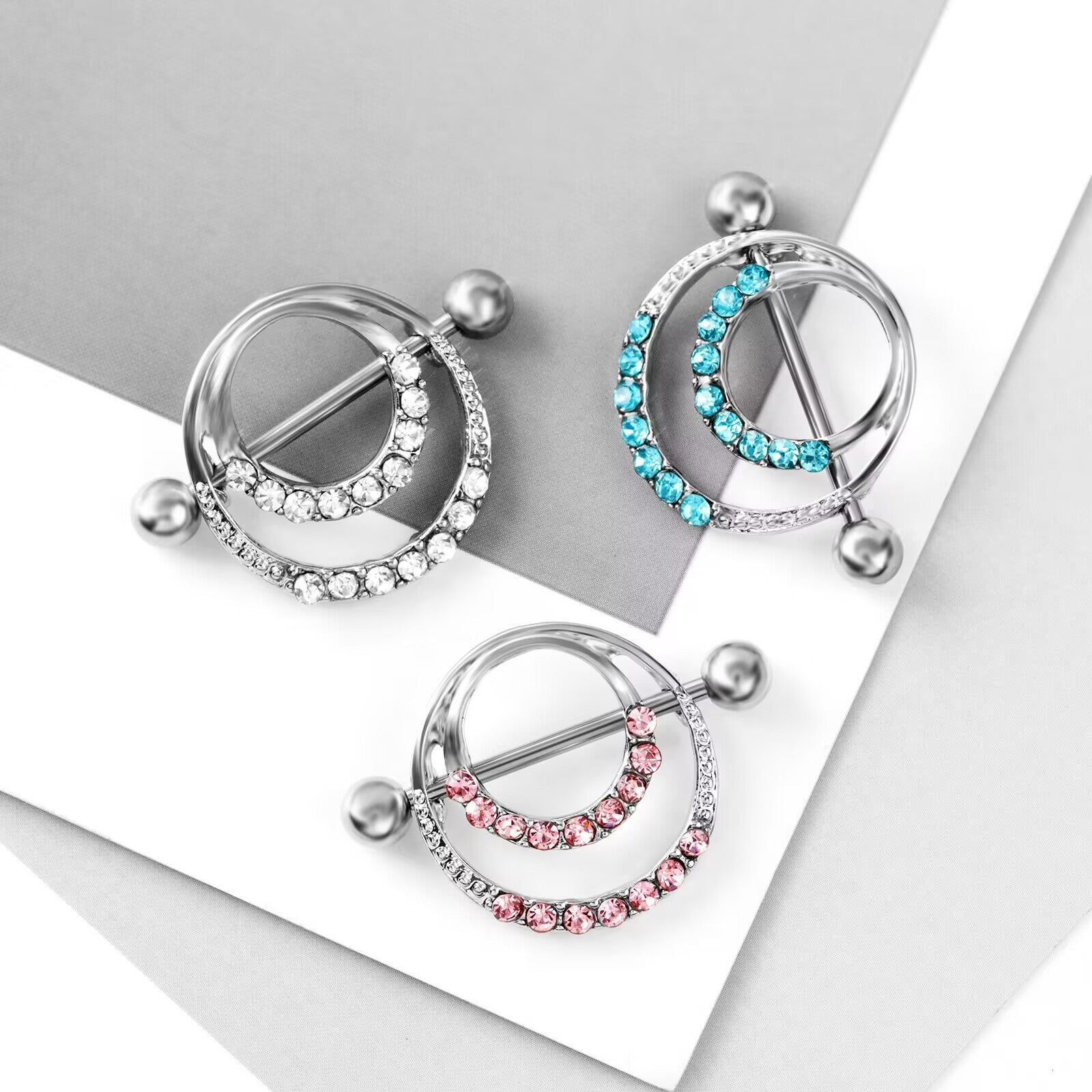 Top view of blue, pink, and white crystal nipple shields arranged on a minimalist surface.