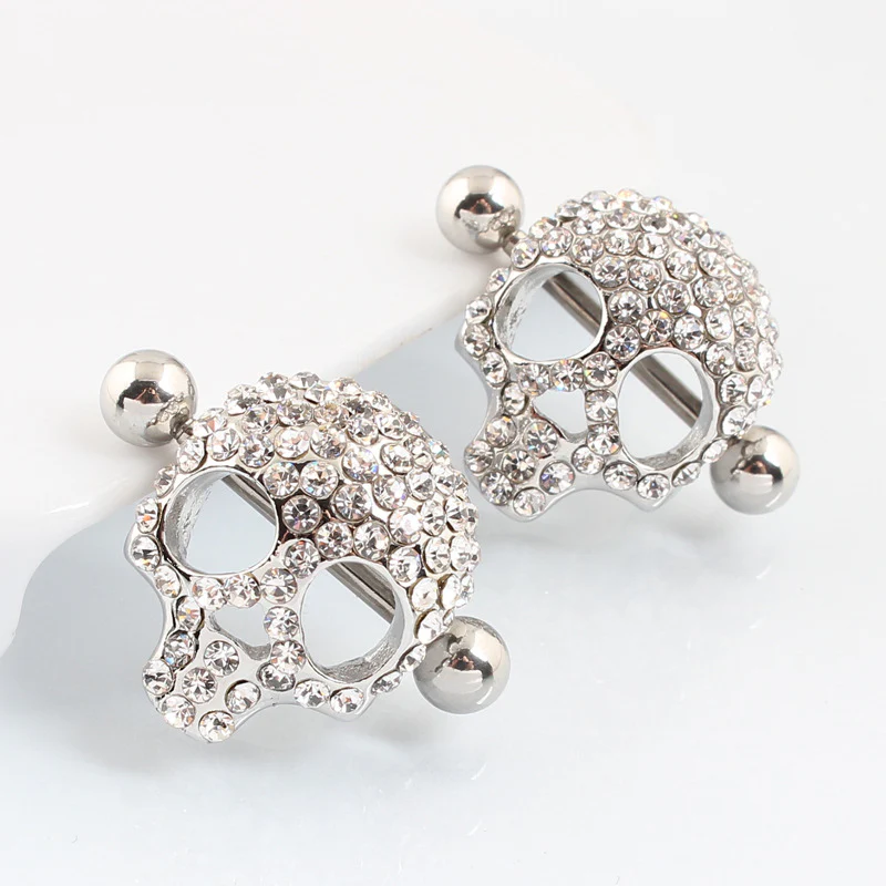 Two silver-toned skull nipple shields with crystals, shown from back-profile angles on a white display surface.